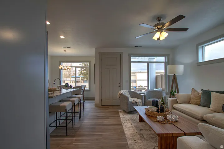 Open-concept living area with wood-finish flooring, a ceiling fan with integrated lighting, and multiple windows