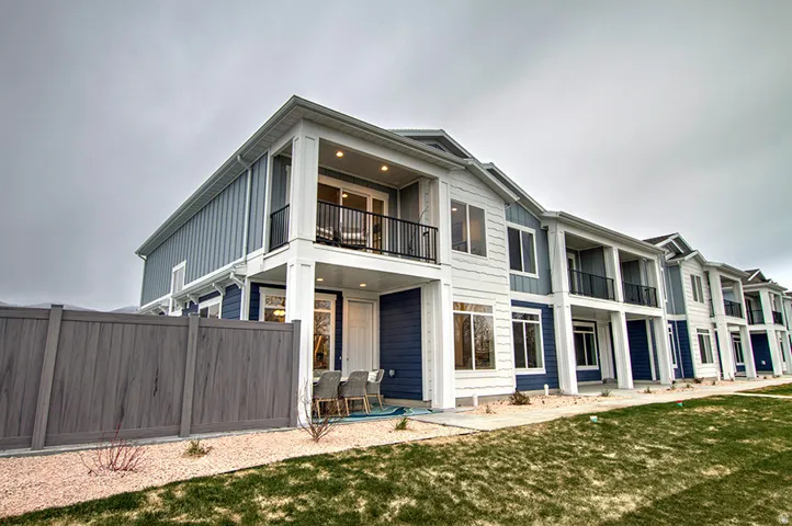 Modern exterior with blue and white siding, covered patio, second-story balcony with black railing, and a private fenced yard