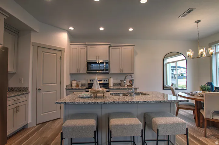 Kitchen with wood-finish flooring, recessed lighting, and a center island featuring a stainless steel sink and integrated dishwasher