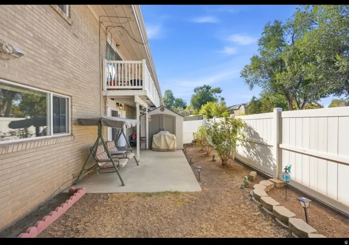 Brick exterior with a second-story balcony, ground-level patio, private fencing, and a built-in storage shed