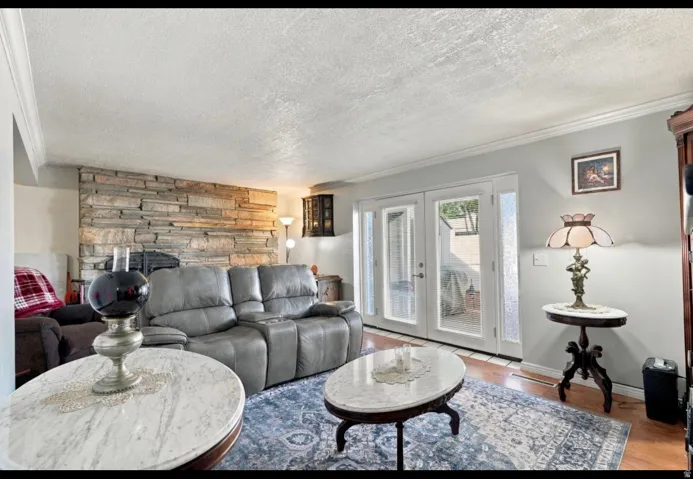Stack stone accent wall, wood flooring, crown molding, white French doors, and side light windows