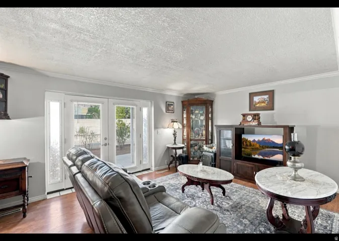 Wood-finish flooring, white wall paint, crown molding, and double glass-paneled doors with frosted sidelights