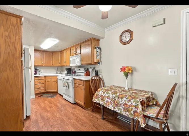 Kitchen featuring wood-finish flooring, wood cabinetry, white appliances, and a compact dining area