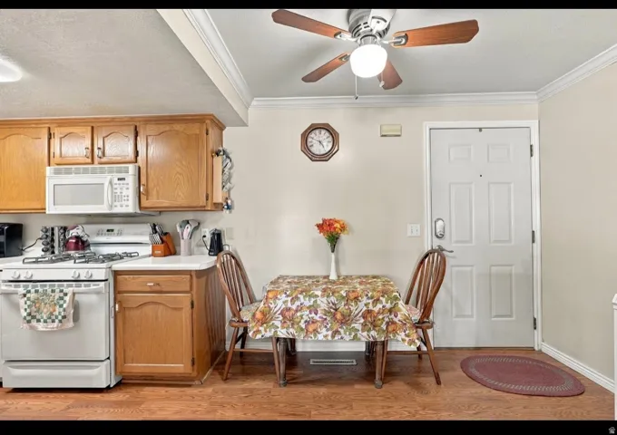 Wood-finish flooring, white paneled entry door, crown molding, ceiling fan with integrated lighting, and wood cabinetry