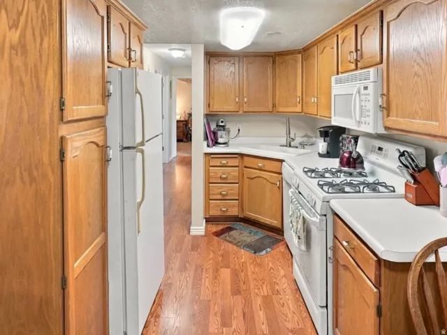 Galley kitchen featuring wood-finish flooring, wood cabinetry, white countertops, and white appliances
