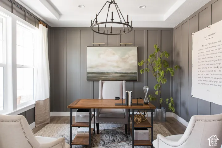 Board and batten wall detailing, wood-finish flooring, two large windows, recessed ceiling lighting, and a prominent chandelier