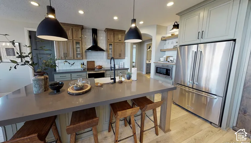 Kitchen featuring a large island with integrated seating, stainless steel French door refrigerator, built-in microwave, and a black range hood over the cooktop