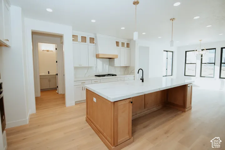Kitchen with light wood-finish flooring, white cabinetry, a large center island with a light countertop, and a black faucet