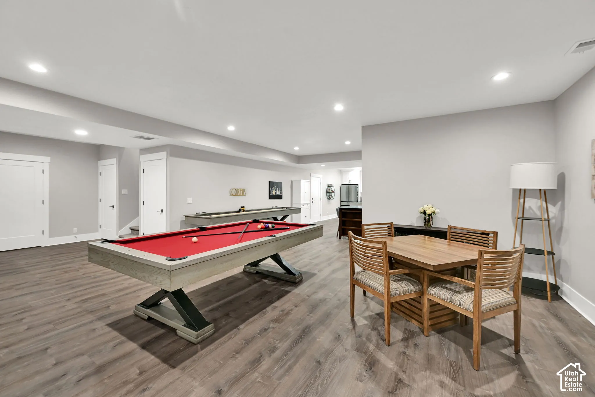 Recessed lighting illuminates wood-finish flooring throughout this expansive recreation space, featuring a negotiable billiard table and a shuffleboard table