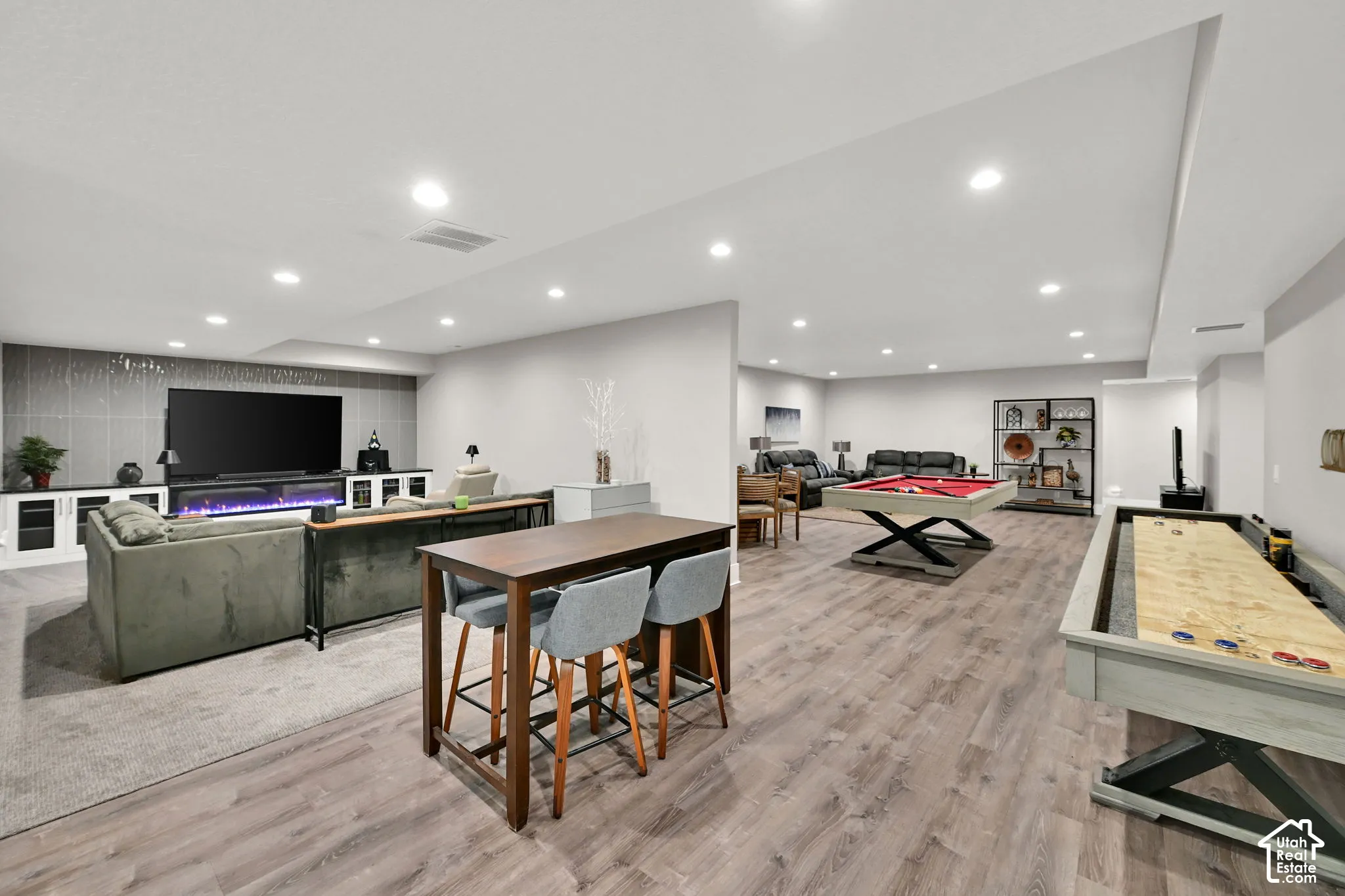 Expansive open-concept recreation space with wood-finish flooring, recessed lighting, and a built-in media center cabinets.