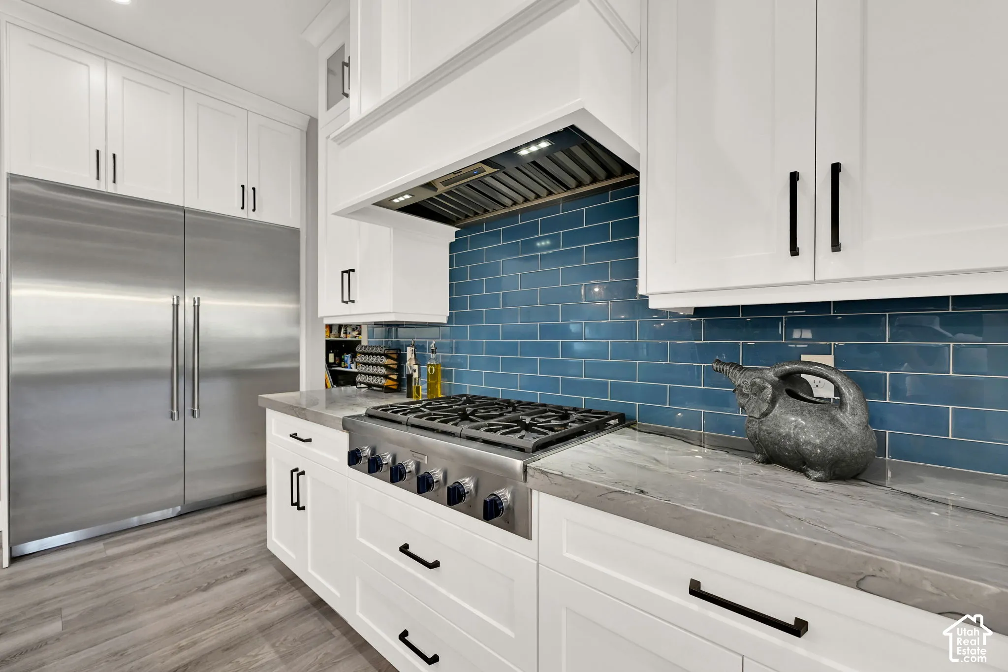 Stainless steel Thermador range with a blue subway tile backsplash, white shaker cabinetry, stainless steel refrigerator, and wood-finish flooring