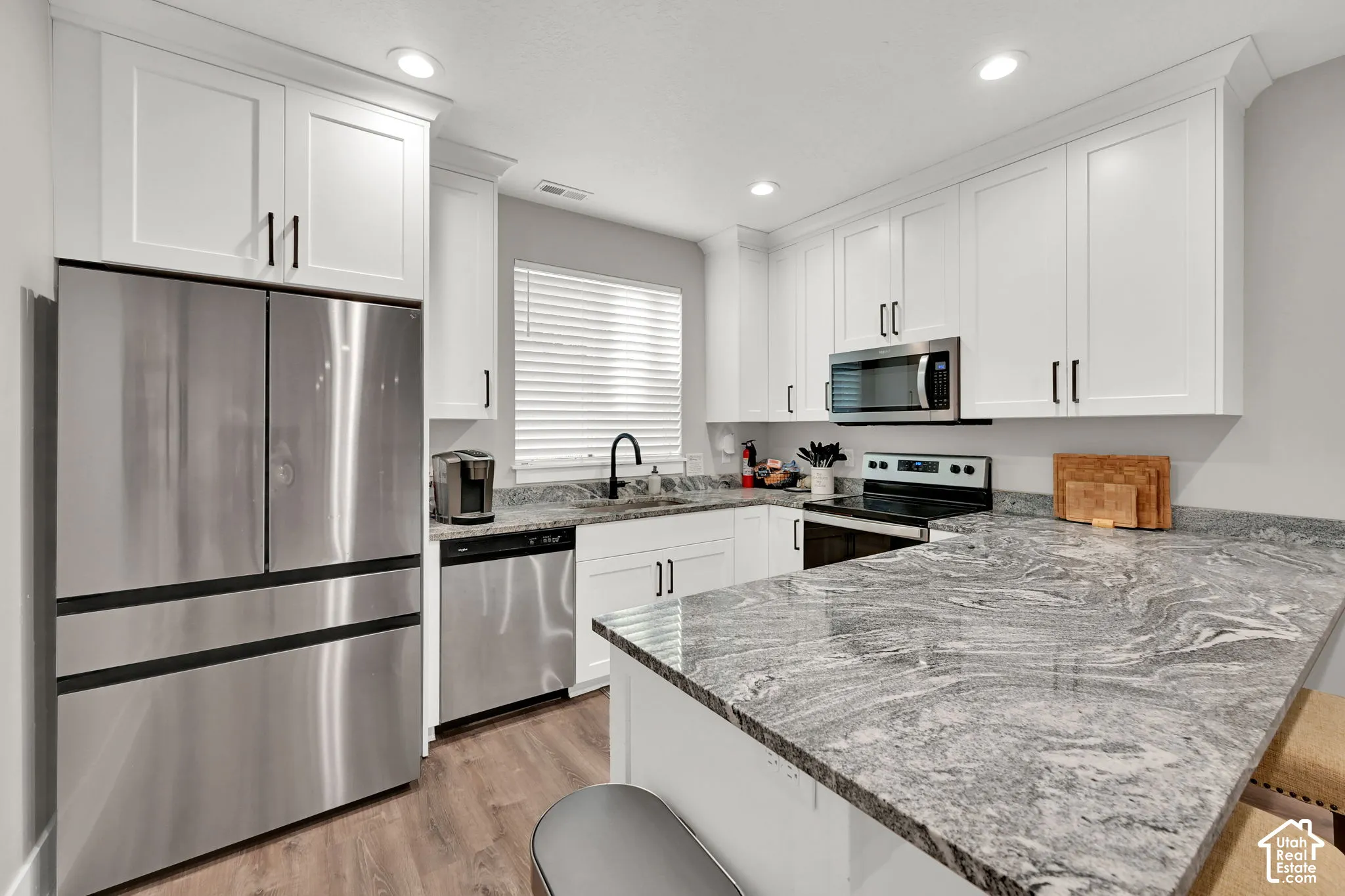 Kitchen featuring white shaker cabinetry, stainless steel appliances, wood-finish flooring, and light-toned patterned countertops