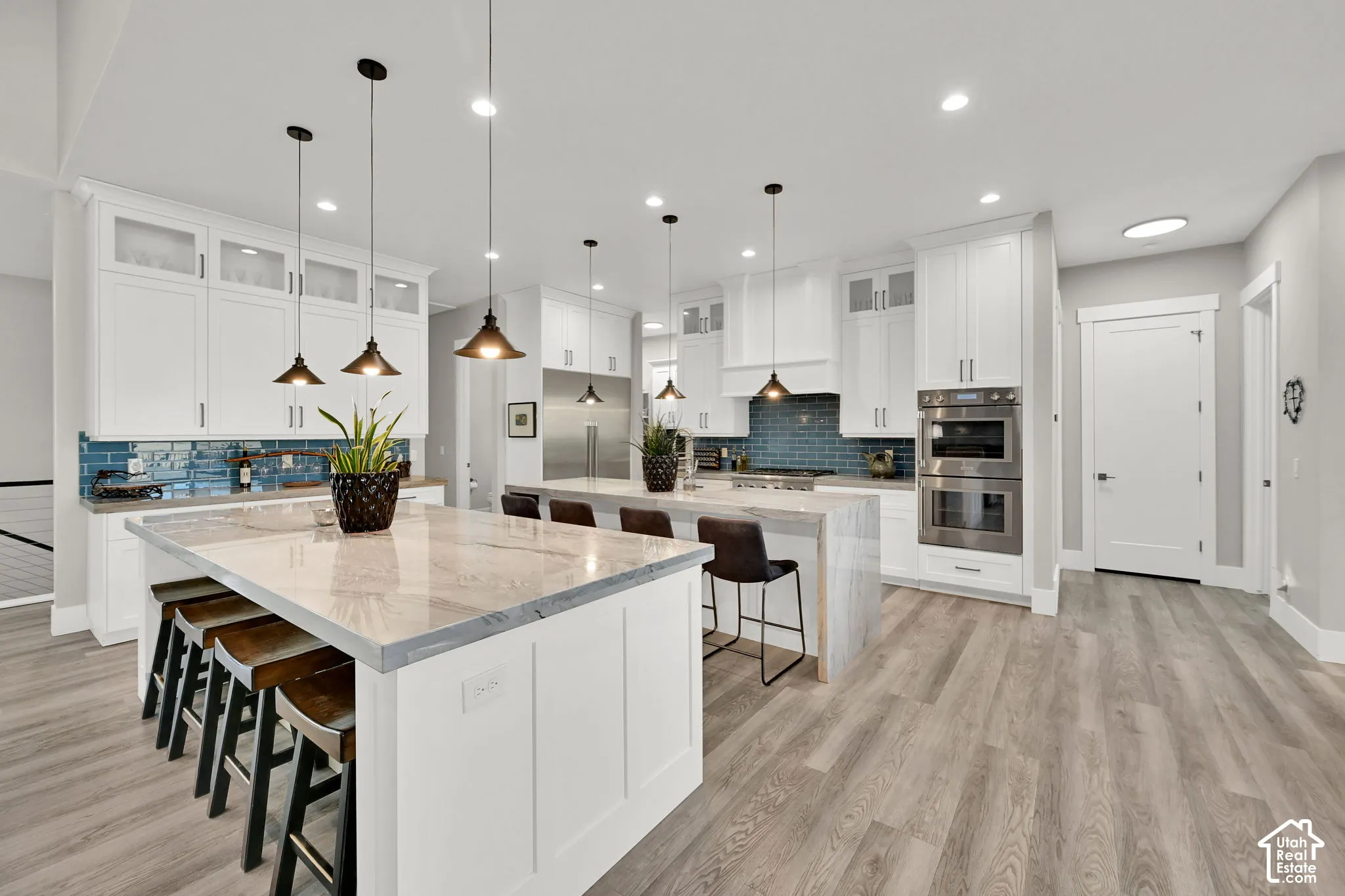 Spacious kitchen featuring two islands with quartz countertops, white cabinetry, a blue tile backsplash, and wood-finish flooring