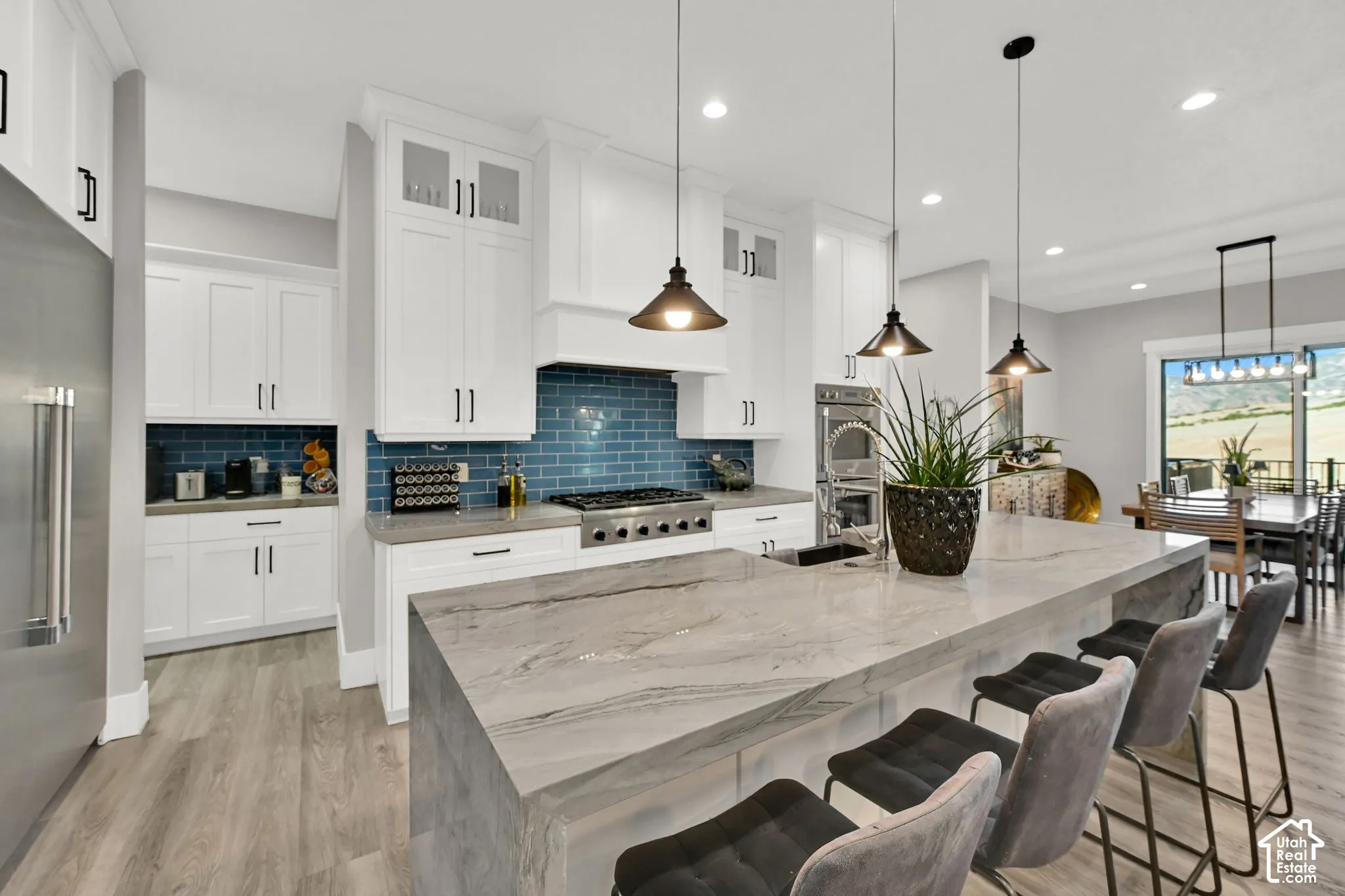 Waterfall island with a quartz countertop,  with all appliances Thermador. wood-finish flooring, white cabinetry, and a blue tile backsplash