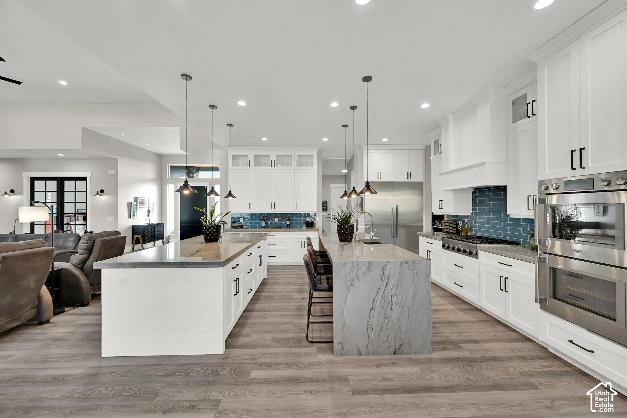 Gourmet kitchen with double islands, stainless steel appliances, crisp white cabinetry, and wood-finish flooring
