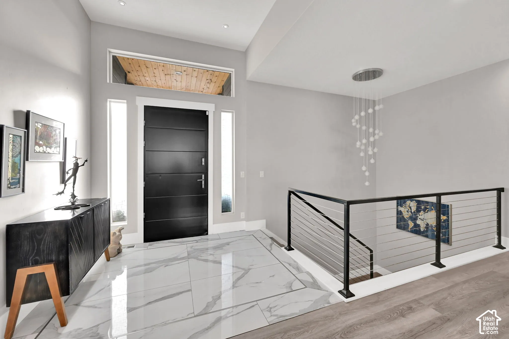 Spacious entryway featuring large marble tile flooring, a modern black entry door with transom window, and a contemporary cable railing system
