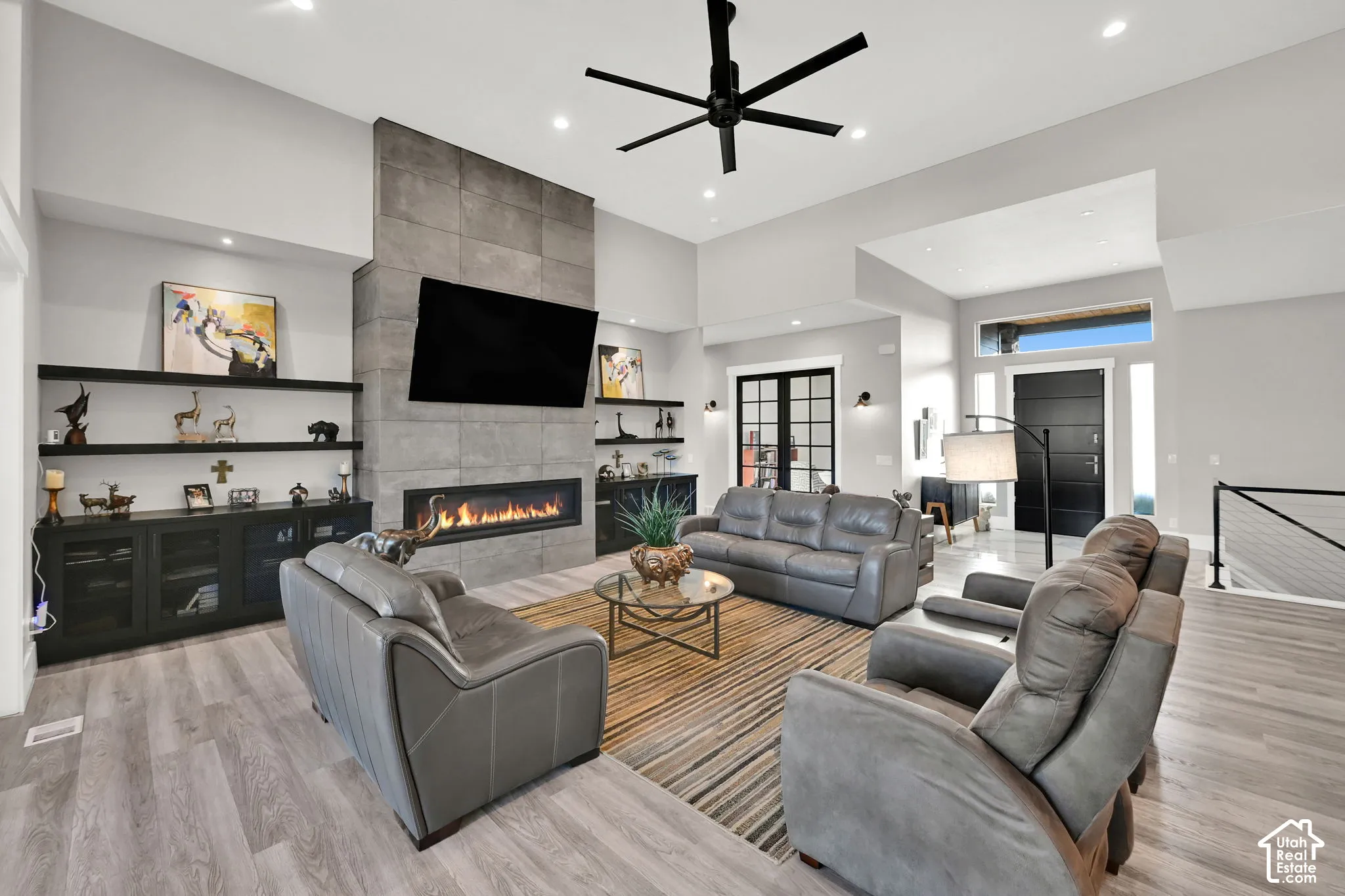 Spacious living area featuring a stone-clad fireplace, wood-finish flooring, built-in shelving, a modern ceiling fan, and recessed lighting