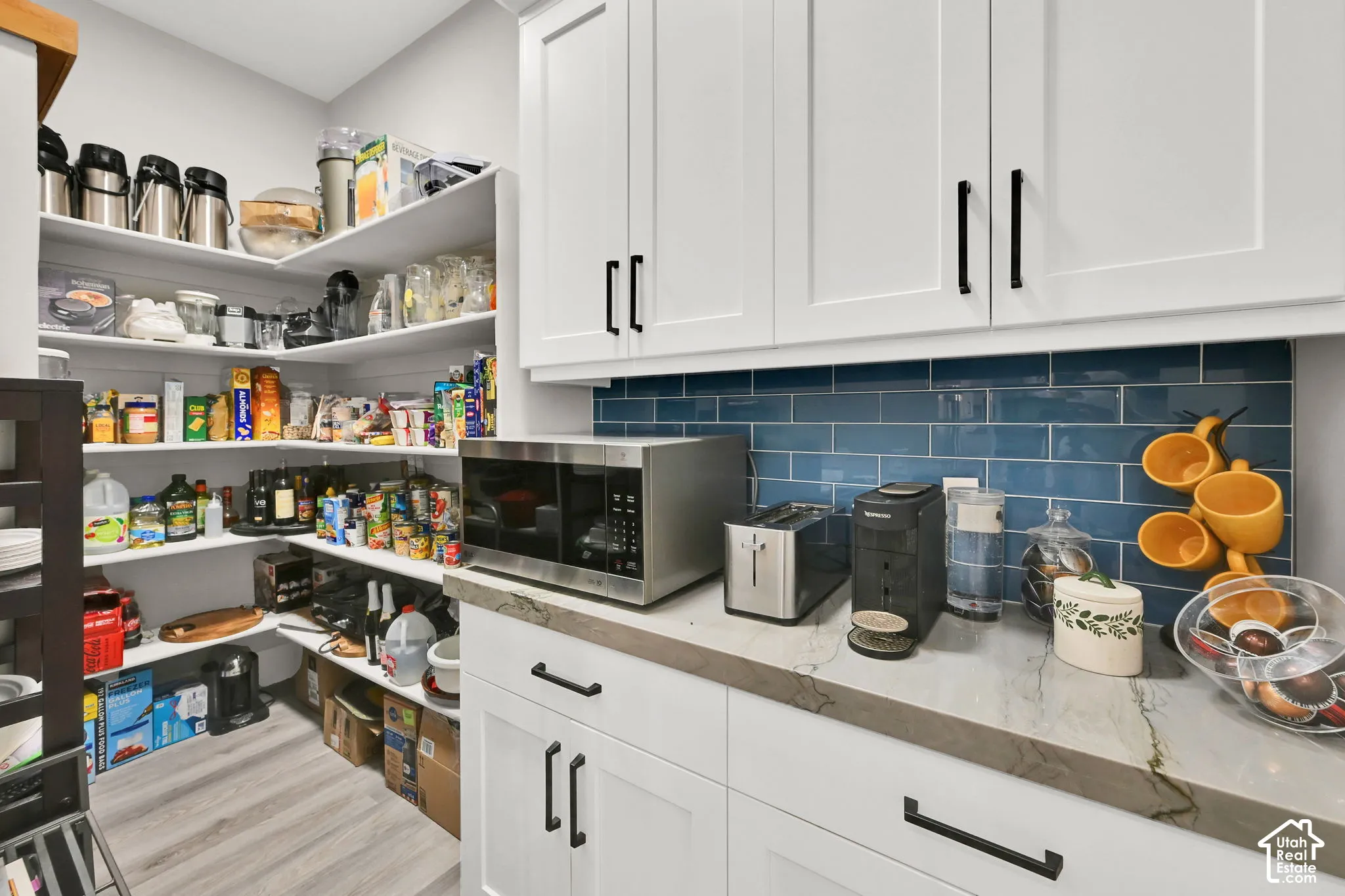 Walk-in pantry with extensive shelving, white cabinetry, a subway tile backsplash, and a quartz countertop