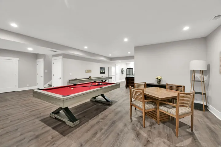 Recessed lighting illuminates wood-finish flooring throughout this expansive recreation space, featuring a billiard table and a shuffleboard table