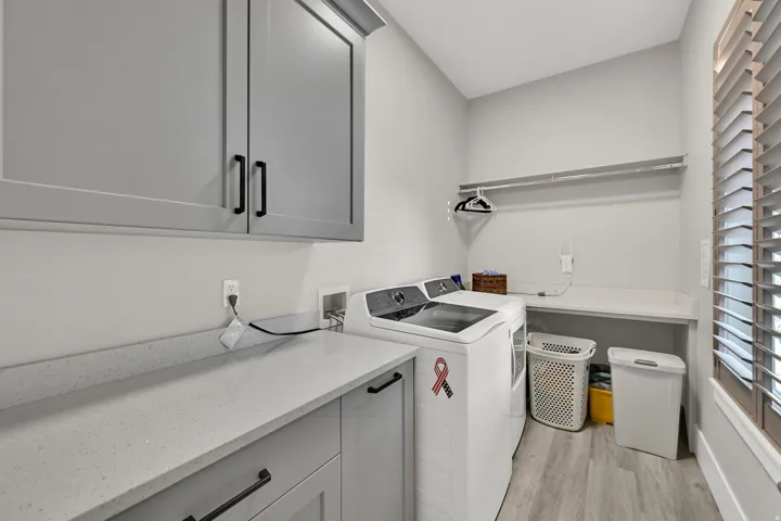 Light gray cabinetry with black hardware, light gray countertops, wood-finish flooring, and a built-in window with horizontal blinds
