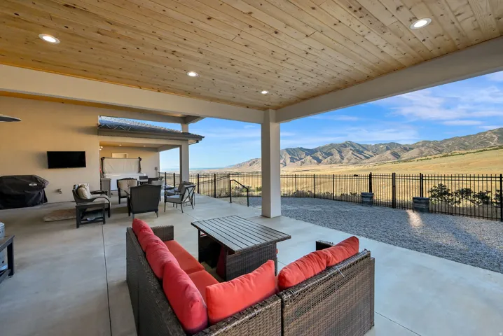 Expansive covered patio with recessed lighting, wood-finish ceiling, concrete flooring, and a black metal fence enclosing the yard
