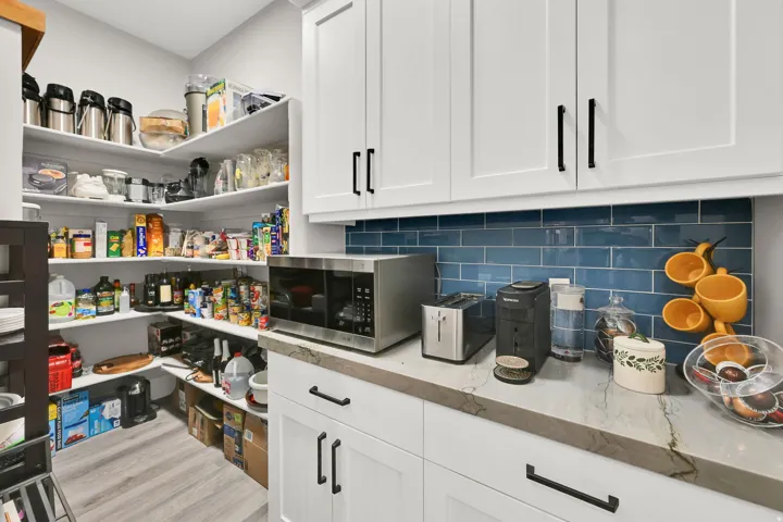 Walk-in pantry with extensive shelving, white cabinetry, a subway tile backsplash, and a stone countertop