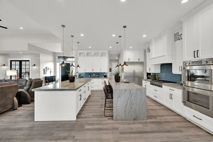 Gourmet kitchen with double islands, stainless steel appliances, crisp white cabinetry, and wood-finish flooring