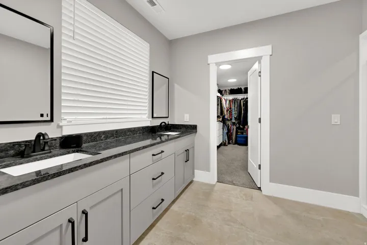 Dual vanities with undermount sinks, dark stone countertops, light gray cabinetry, and matte black fixtures