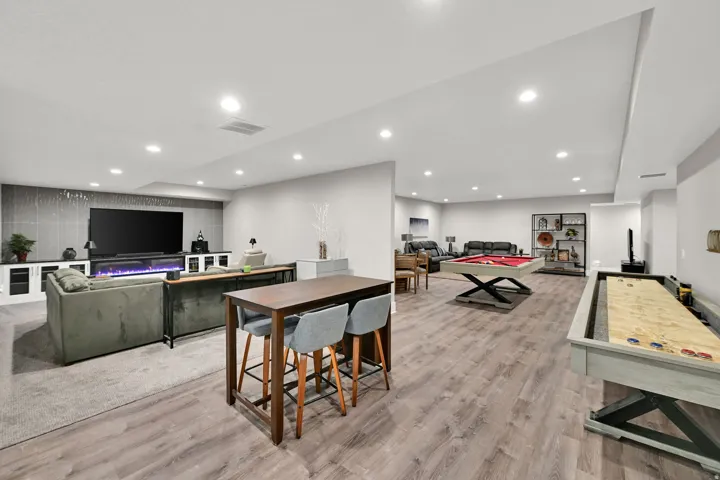 Expansive open-concept recreation space with wood-finish flooring, recessed lighting, and a built-in media center with a linear fireplace