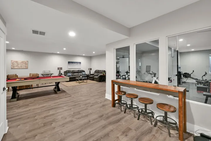 Spacious lower-level area featuring recessed lighting, wood-finish flooring, and a built-in wood bar with stools