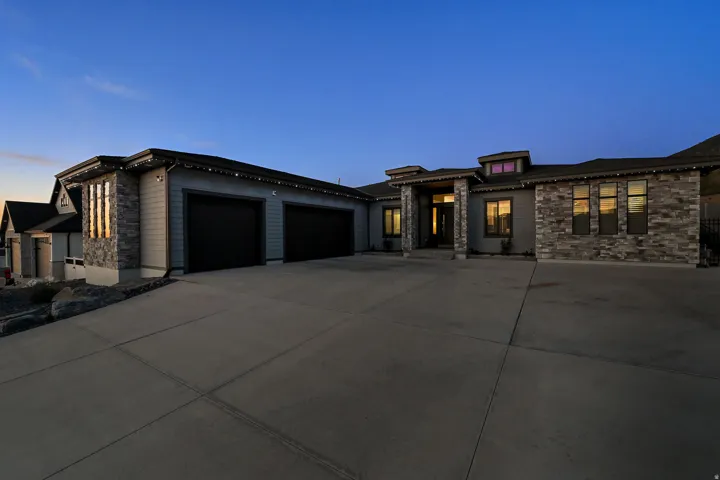 Exterior featuring stone and siding finishes, a two-car garage with dark doors, a covered entry, and a concrete driveway