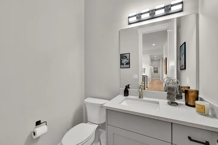 Recessed sink basin, stone-finish countertop, vanity with panel cabinetry, wall-mounted light fixture, and toilet