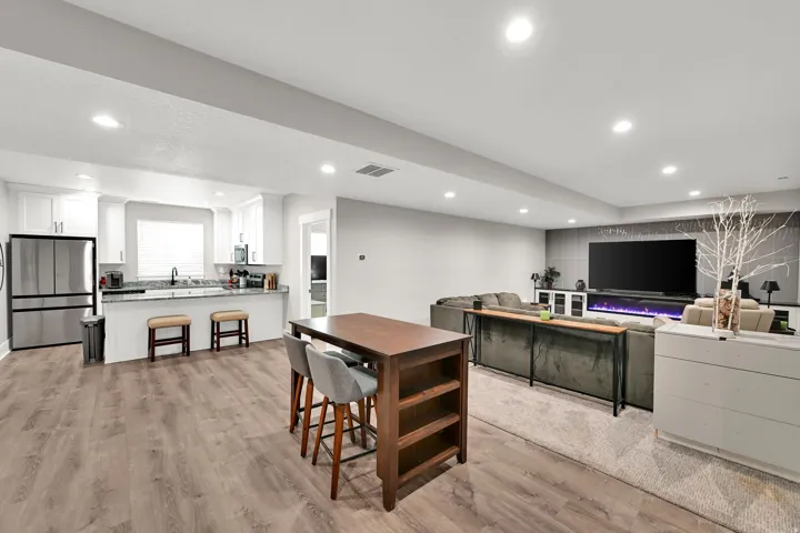 Open-concept living space with wood-finish flooring, recessed lighting, white cabinetry, a kitchen island with seating, and a feature wall with a built-in fireplace