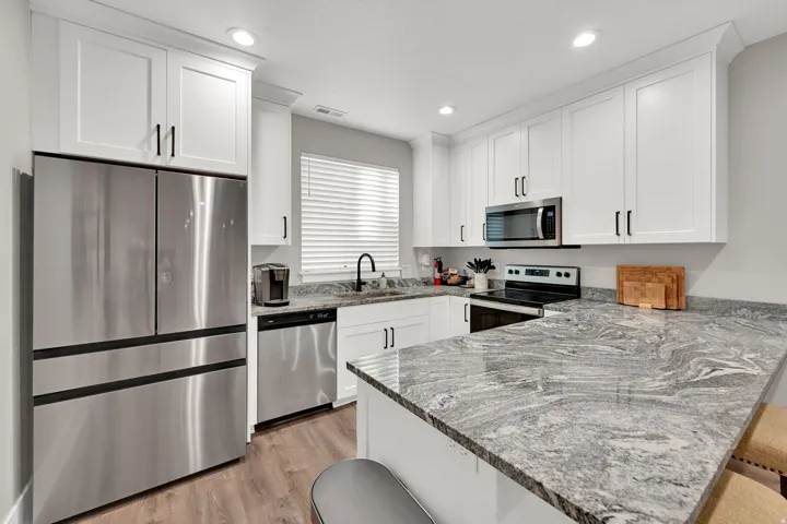 Kitchen featuring white shaker cabinetry, stainless steel appliances, wood-finish flooring, and light-toned patterned countertops