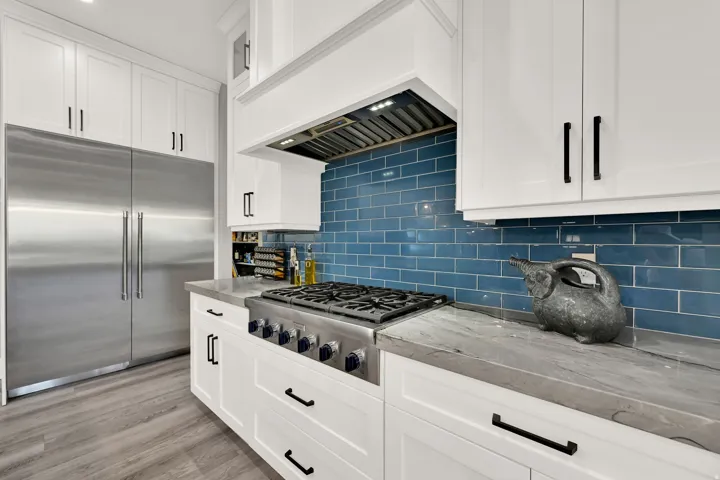 Stainless steel Thermador range with a blue subway tile backsplash, white shaker cabinetry, stainless steel refrigerator, and wood-finish flooring