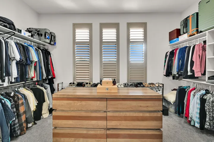 Spacious master walk-in closet featuring central wood-finish island with drawers, extensive wire shelving, multiple hanging rods, and three windows with plantation shutters