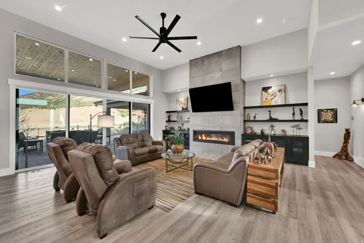 Vaulted ceiling with a contemporary ceiling fan, full-height tile-clad fireplace, built-in shelving, large sliding glass doors, and wood-finish flooring