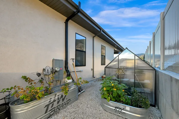 Stucco exterior with black-framed windows, gravel ground cover, and metal raised garden beds and green house.
