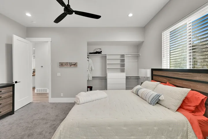 Recessed lighting, ceiling fan, built-in closet organization system, large window with blinds, and wood-finish headboard