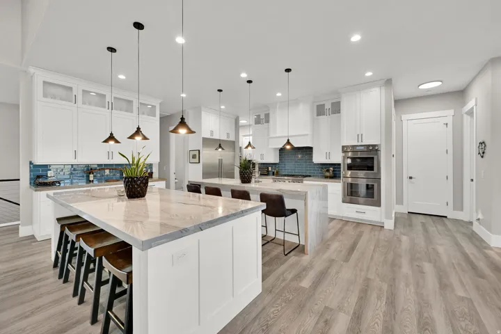 Spacious kitchen featuring two islands with stone countertops, white cabinetry, a blue tile backsplash, and wood-finish flooring