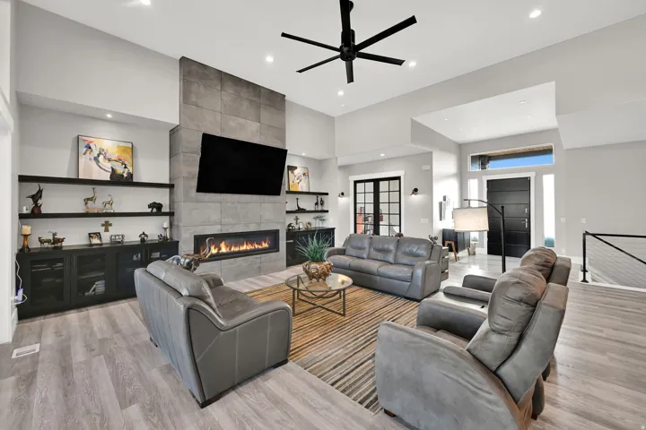 Spacious living area featuring a stone-clad fireplace, wood-finish flooring, built-in shelving, a modern ceiling fan, and recessed lighting