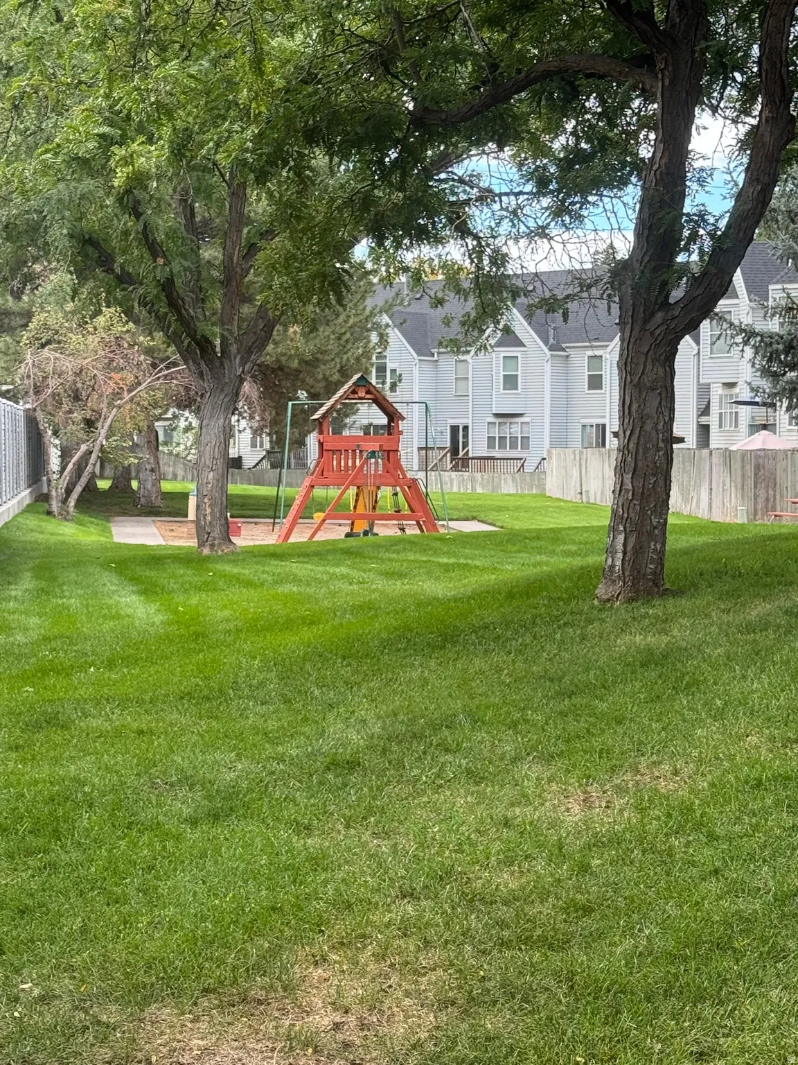 Landscaped common area featuring mature trees, a wooden play structure, and green lawn space