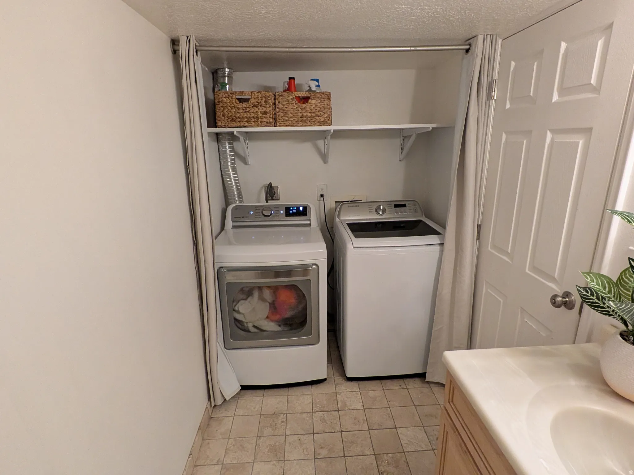 Recessed laundry area with overhead shelving and light-toned floor tiles