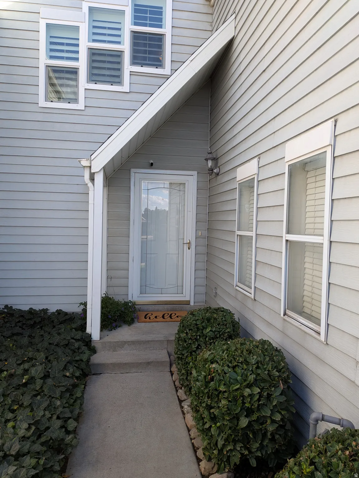 Light gray siding exterior with white window frames and a glass-paneled entry door