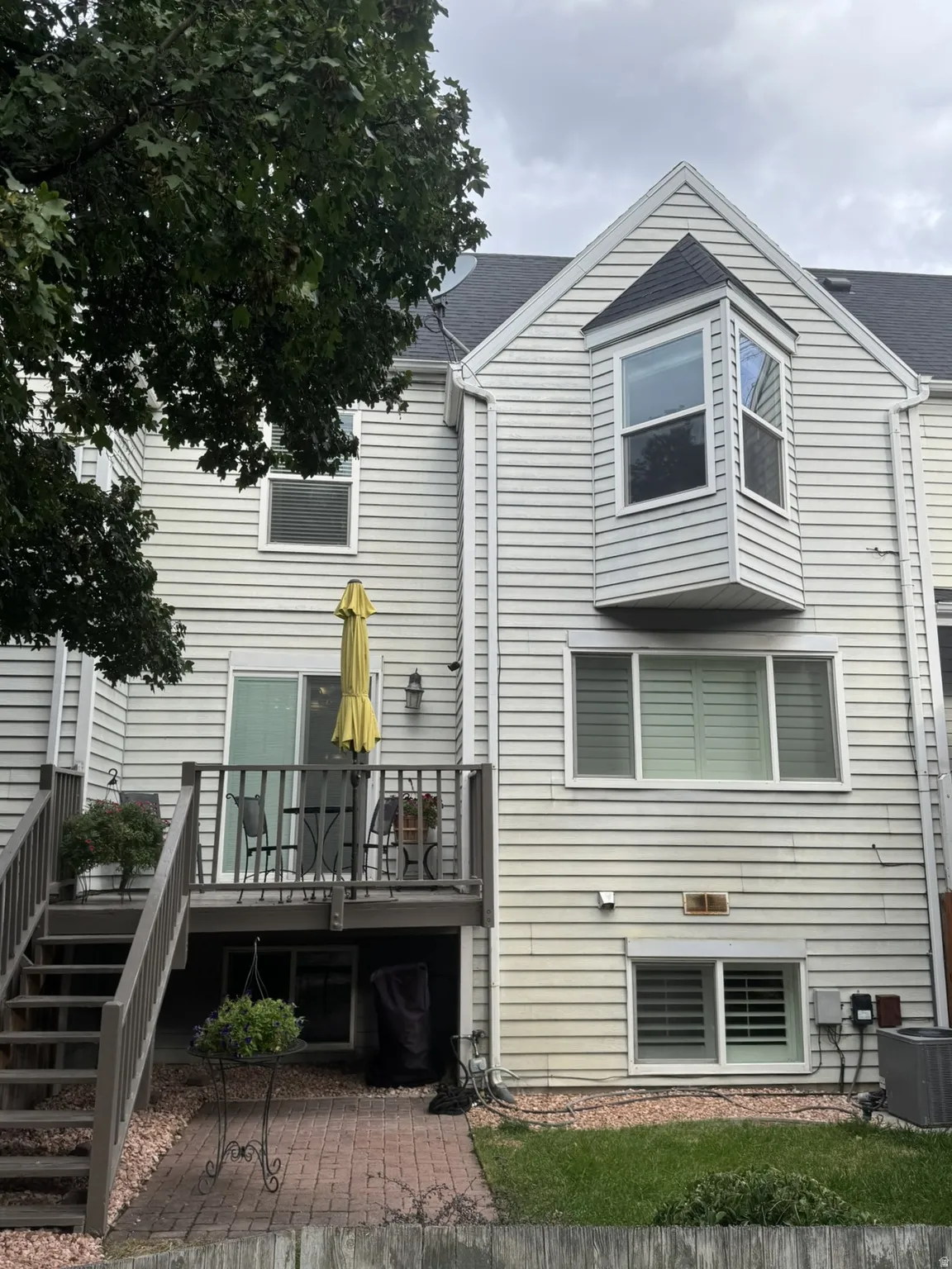Rear exterior featuring a multi-level deck with stairs, a brick patio, and a grass area