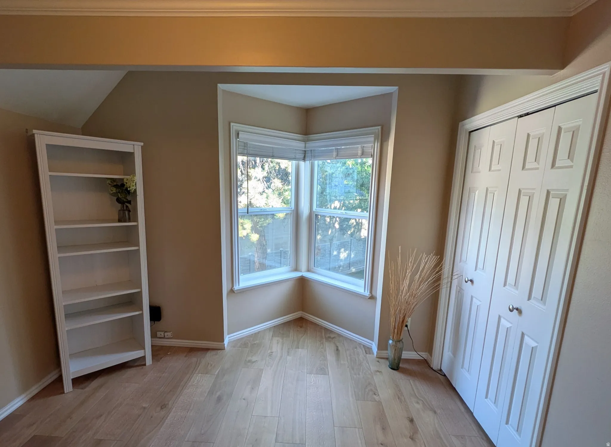 Wood-finish flooring, corner bay window, crown molding, and bifold closet doors