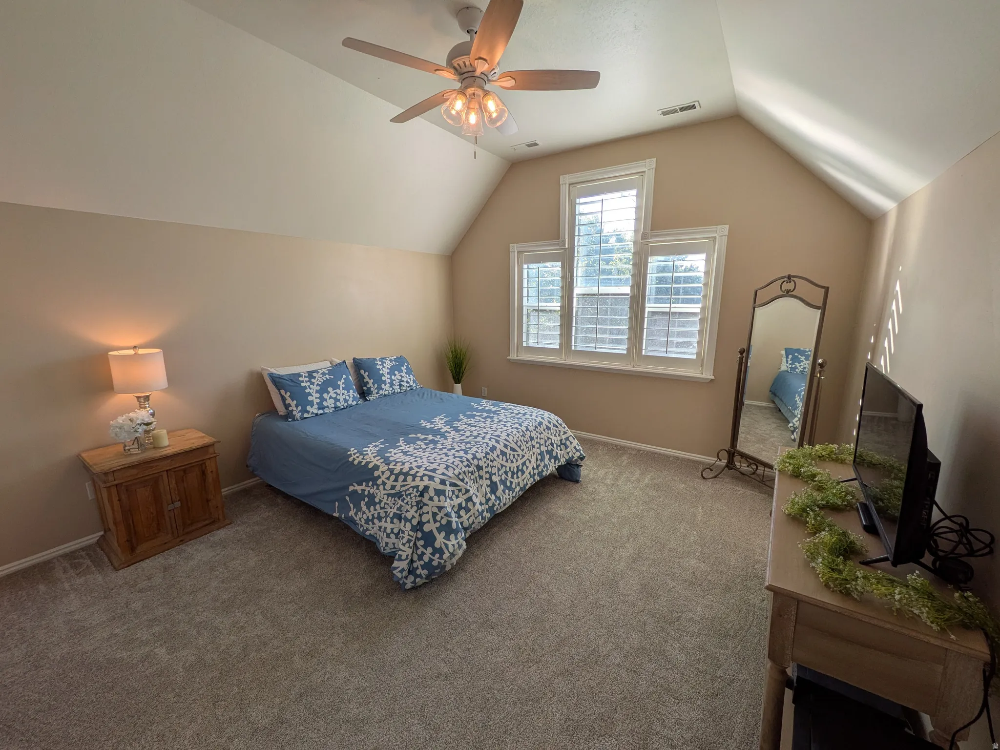Vaulted ceiling, carpeted flooring, ceiling fan, multiple windows with blinds, and neutral wall tones
