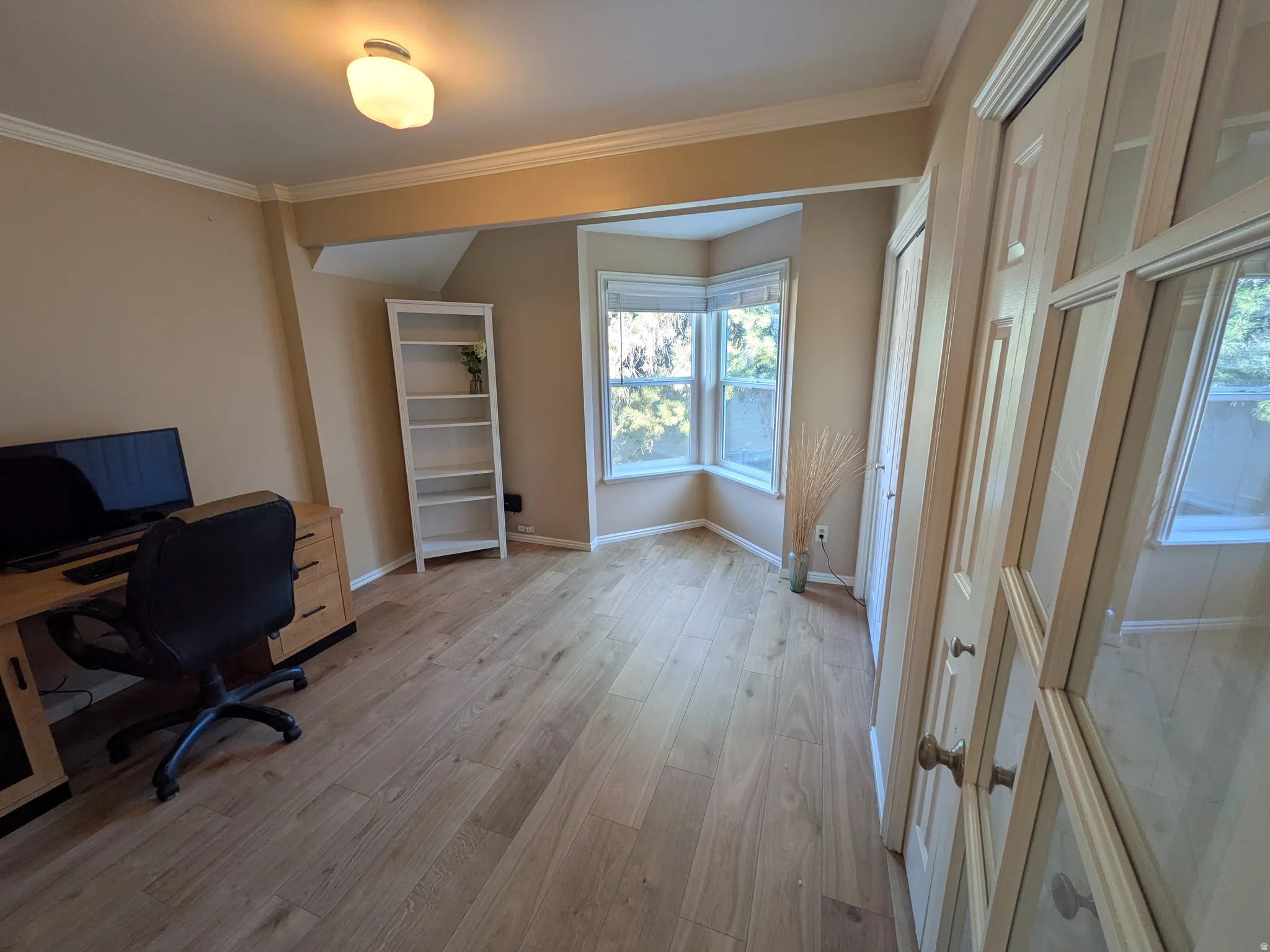 Hardwood-style flooring, bay window, permanent ceiling light fixture, crown molding, and a paneled closet door