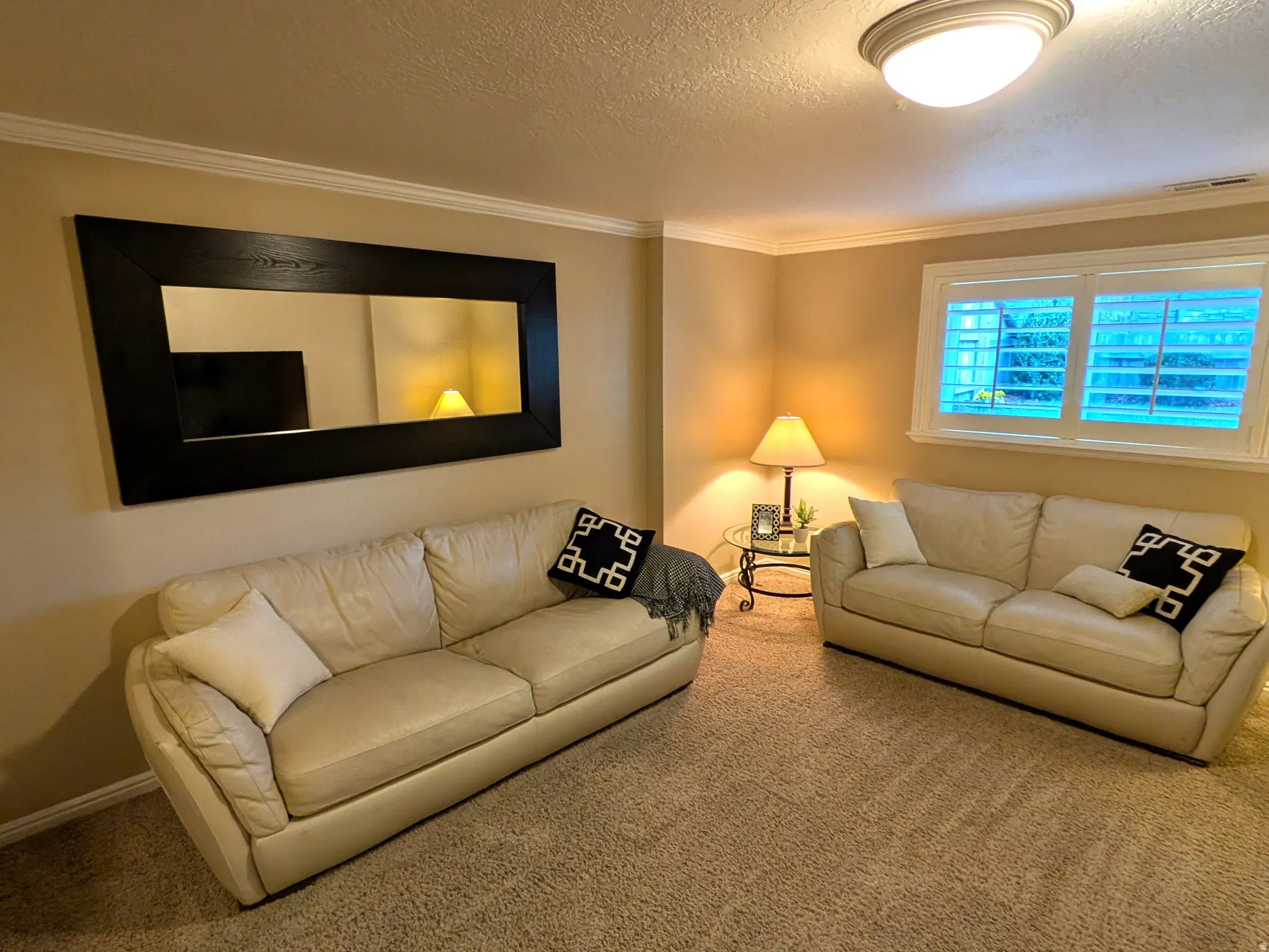 Warm interior lighting, crown molding, a large framed mirror, and plantation window shutters