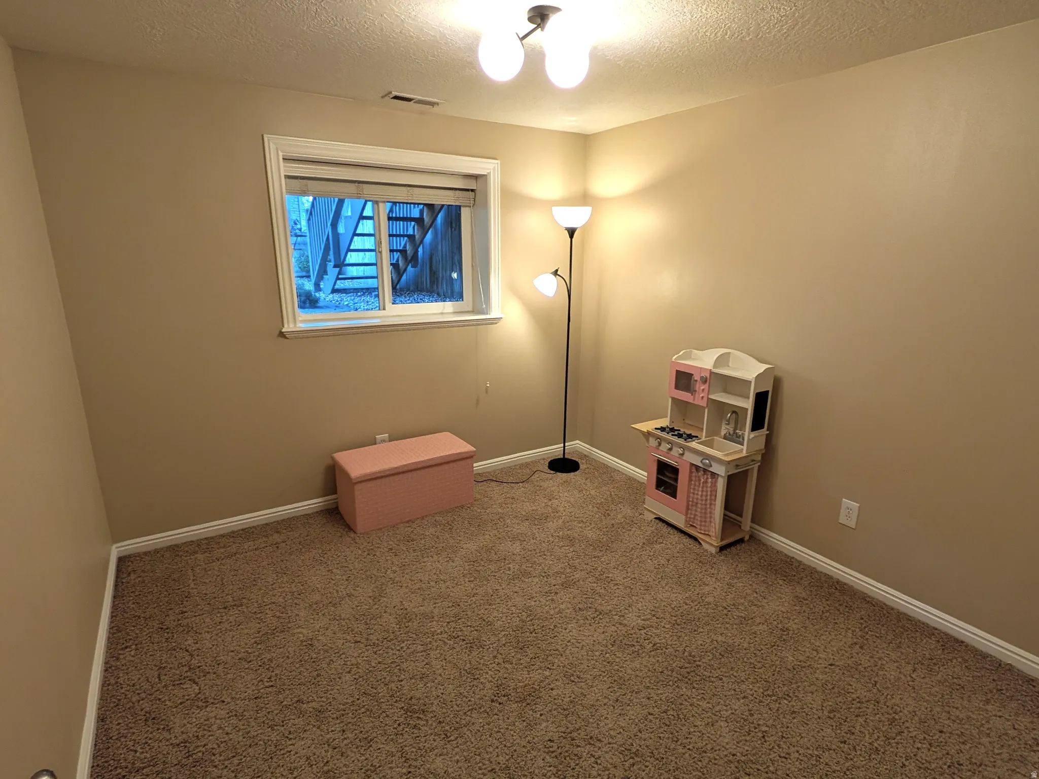 Carpeted room featuring a window with white trim, tan wall paint, and a ceiling-mounted light fixture